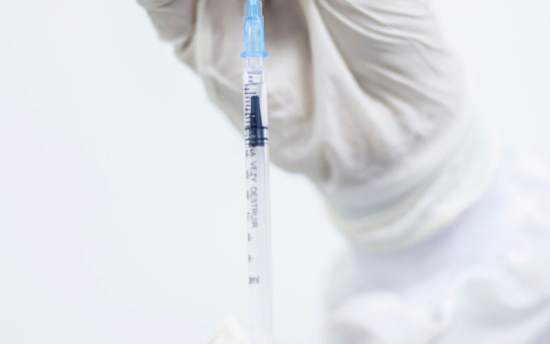 Hands drawing liquid from a vial into a syringe.