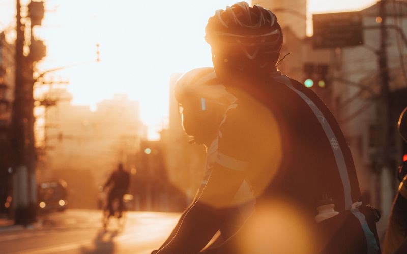 A cyclist rides through city streets at sunrise.